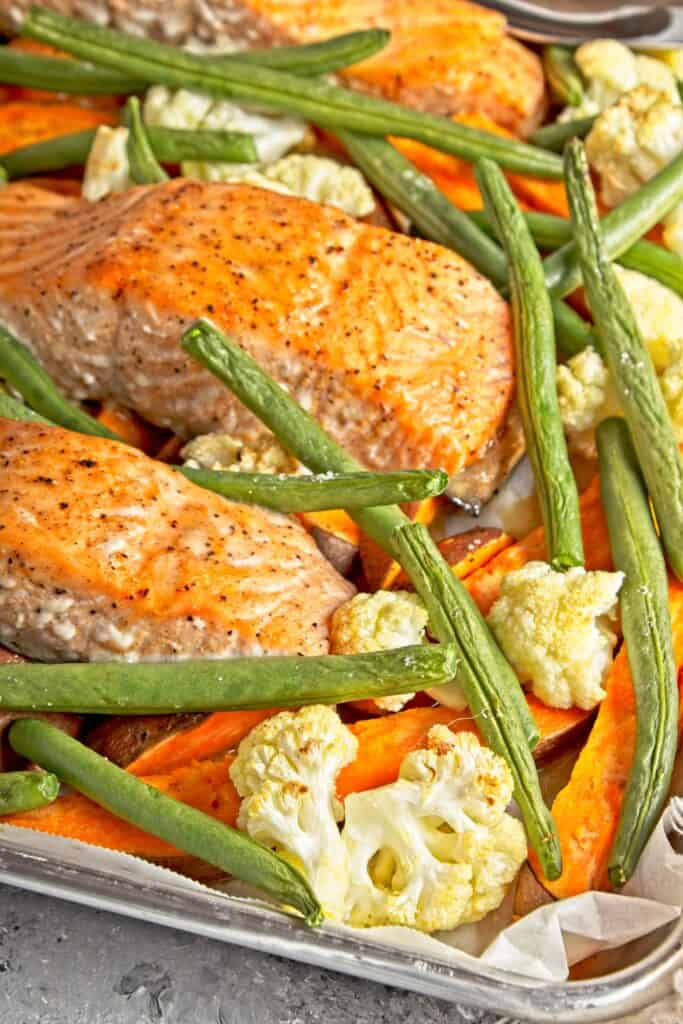 Side view of cooked sheet pan salmon and veggies meal including green beans, cauliflower, and sweet potatoes displayed on the sheet pan.